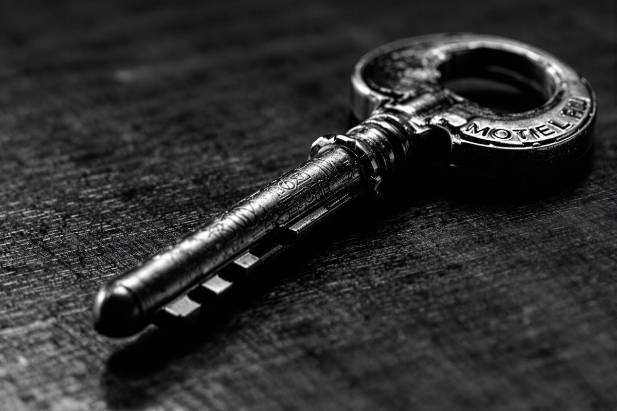 Llave de habitación de latón con llavero de peso sobre el mostrador pulido
            de recepción, con luz rasante marcando el metal gastado.